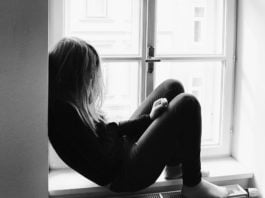 Biało-czarne zdjęcie, na którym smutna dziewczyna siedzi na parapecie